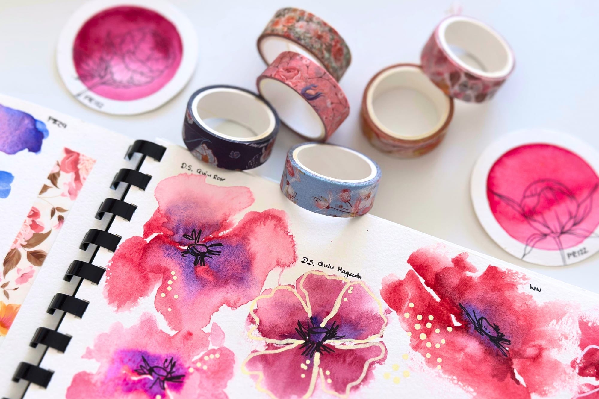 Floral washi tape rolls next to watercolor sketches in a sketchbook