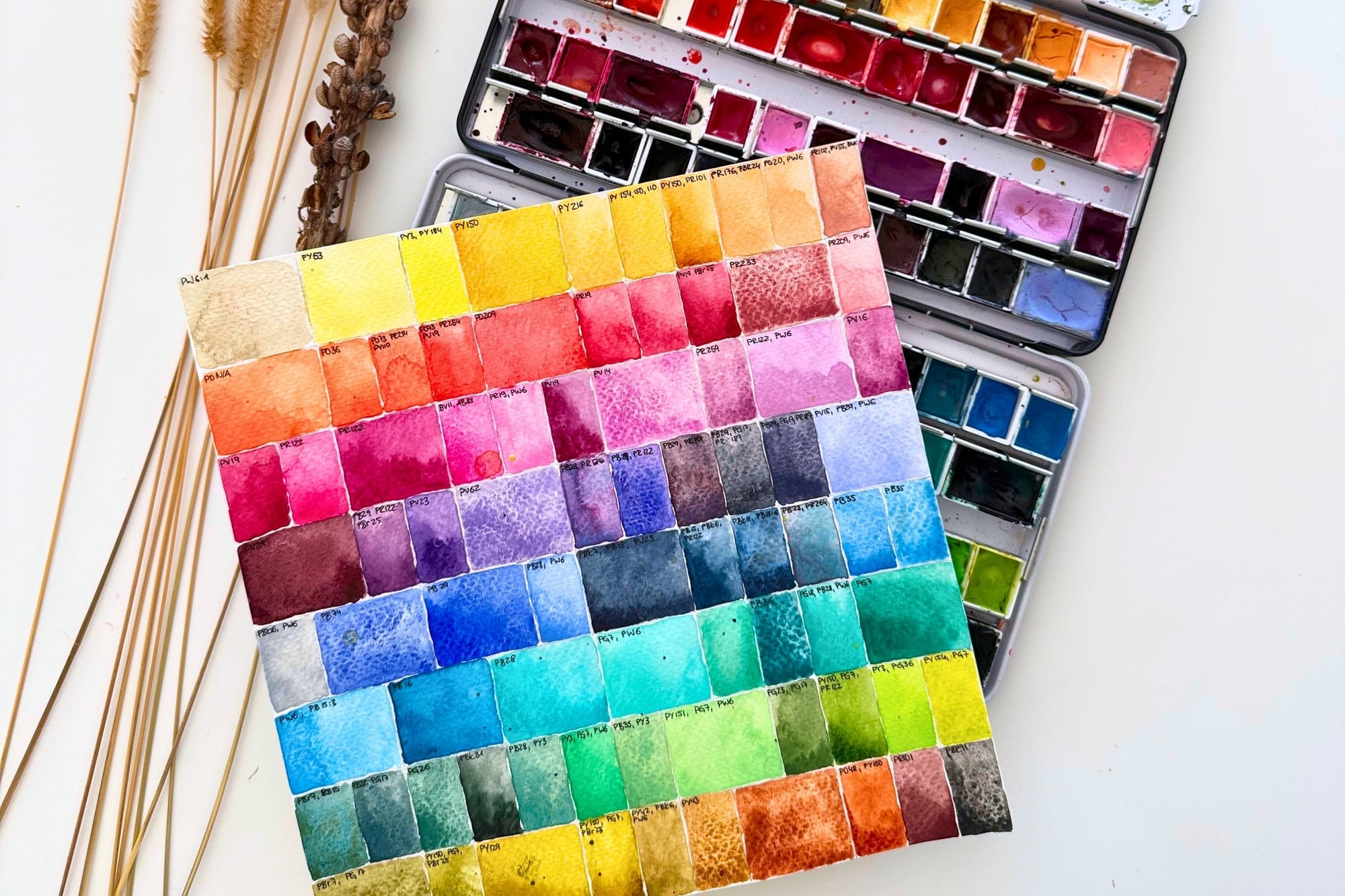 A hand-painted color chart with many pigment swatches next to two watercolor tins